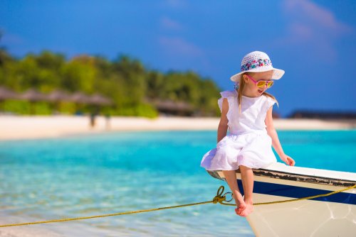 Niña sentada en un barco en la orilla de la playa a punto de salir a navegar.