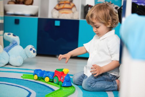 Niño de dos años jugando en el suelo con un tren de juguete.