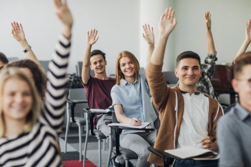 Alumnos con las manos levantadas con ganas de aprender.