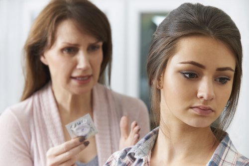 Madre hablando con su hija preadolescente sobre educación sexual con un preservativo de la mano.