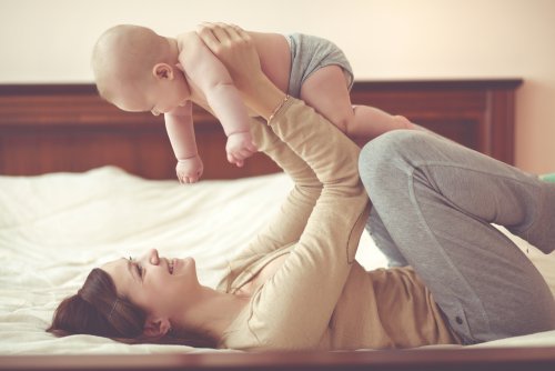 Mamá jugando con su bebé en la cama para estimular el desarrollo de los sentidos.