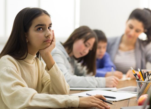 Niña estudiante distraída en clase debido a que no ha tenido tiempo de descanso frecuente en toda la mañana de clase.