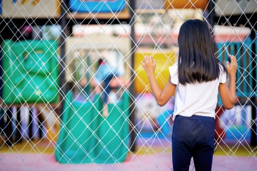 Niña víctima de abusos mirando a través de una valla cómo juegan unos niños en el parque.