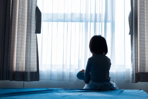 Niña víctima de abuso infantil mirando por la ventana.