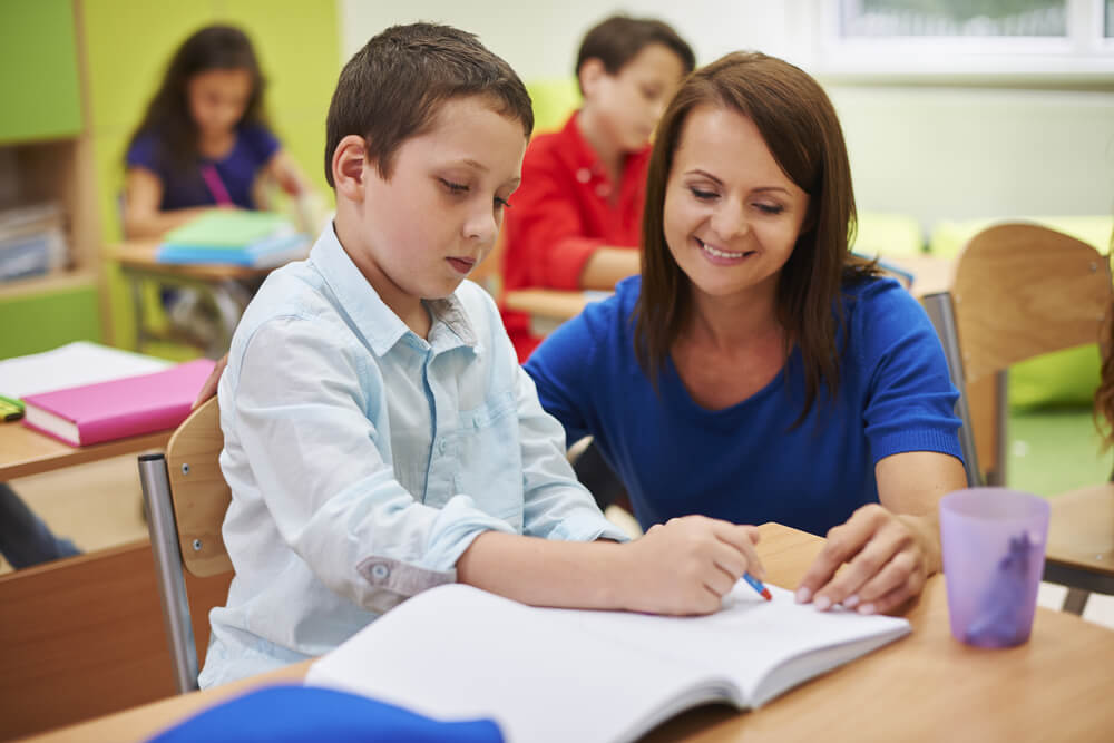 Niño en clase necesitando la ayuda de su profesora.