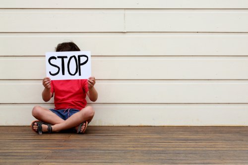 Niño con un cartel de stop para que pare el abuso infantil.