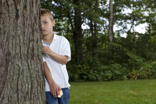 Niño tímido e introvertido escondido detrás de un árbol porque no juega con nadie en el colegio.