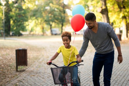 Niña montando en bici con su padre al lado a modo de refuerzo positivo.