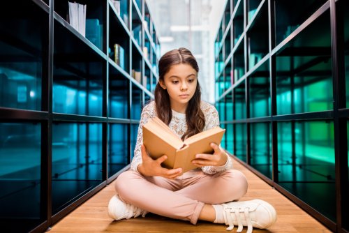 Niña leyendo un cuento con varios finales sentada en el suelo de una biblioteca.