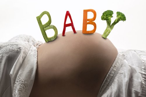 Mujer embarazada con palabra 'baby' en la barriga escrita con comida.