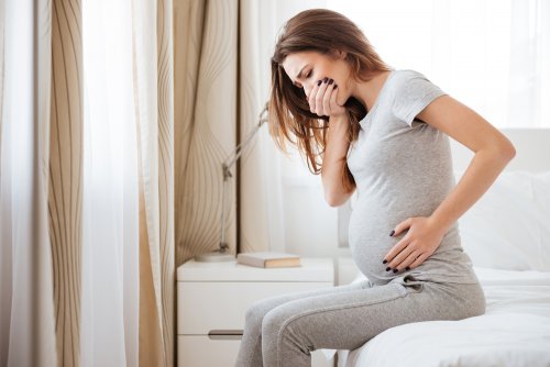 Mujer embarazada sentada en la cama con náuseas y vómitos antes de empezar con el tratamiento.