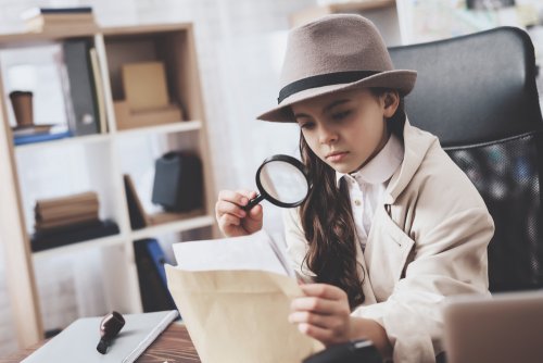 Niño detective mirando un papel con una lupa.