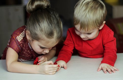 Niña pintándole las uñas a otro niño de rojo.