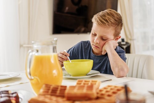 Niño desayunando muy triste decepcionado porque no ha conseguido entrar en el equipo de fútbol que quería.
