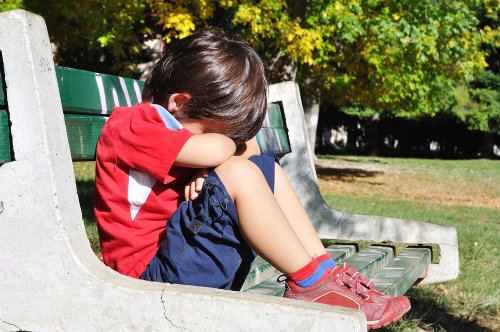 Niño triste sentado en un banco del parque porque no le han invitado al cumpleaños.