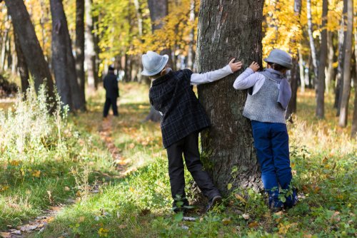 Niños detectives observando detrás de un árbol.