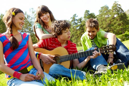 Adolescente tocando la guitarra para sus amigos en el campo.