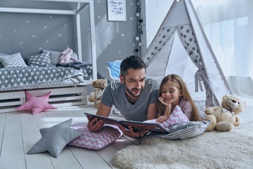 Padre leyendo con su hija tumbados en el suelo de la habitación.