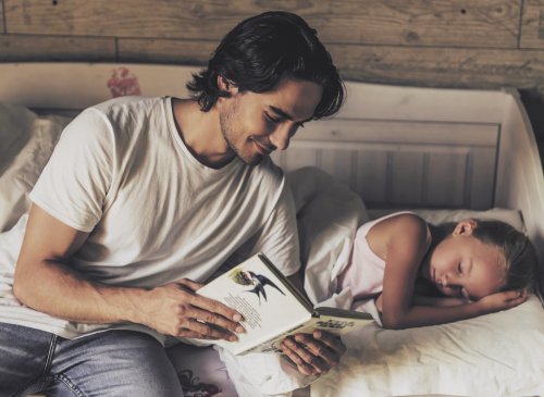 Padre aplicando los tips para contar un buen cuento mientras le lee a su hija en la cama.