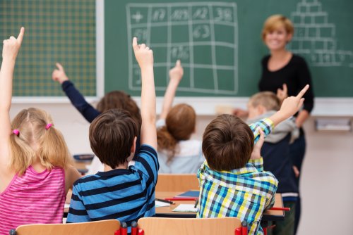 Alumnos levantando la mano en clase para preguntar a la profesora.