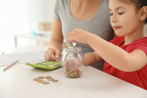 Niña metiendo monedas en un bote con su madre para aprender a ahorrar.