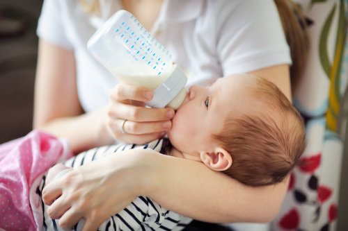 Madre asumiendo los riesgos de la lactancia artificial dándole un biberón a su bebé.