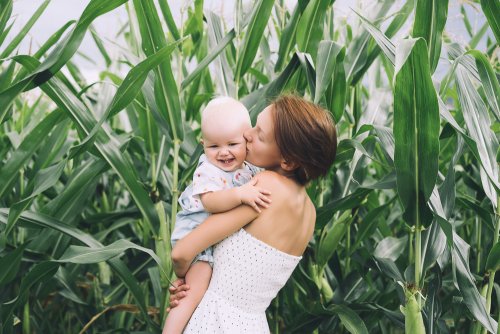 Mamá con su bebé en brazos dándole un beso en el campo.