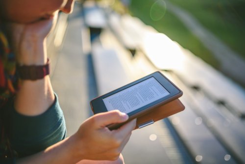 Mujer usando plataformas de lectura digital en su libro electrónico para leer al aire libre.