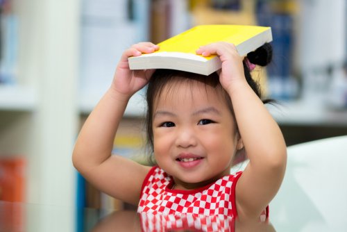 Niña bebé con un libro sobre la cabeza en una bebeteca.