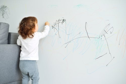 Niña pintando la pared del salón.
