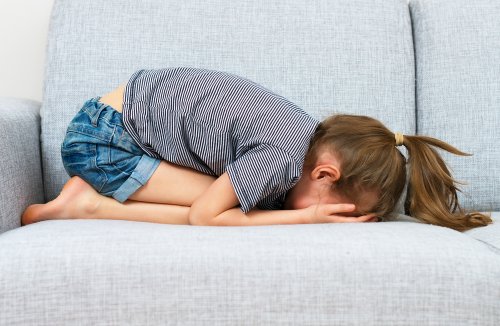 Niña llorando en el sofá con atiquifobia, miedo al fracaso.