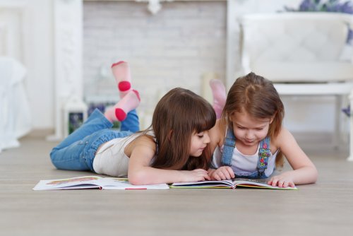 Niñas leyendo tumbadas en el suelo libros infantiles para aprender las letras.