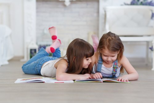 Niñas leyendo tumbadas en el suelo libros infantiles para aprender las letras.