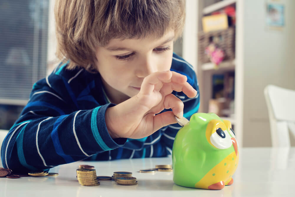 Niño metiendo dinero en la hucha como parte de una de las responsabilidades que puede asumir con su edad.