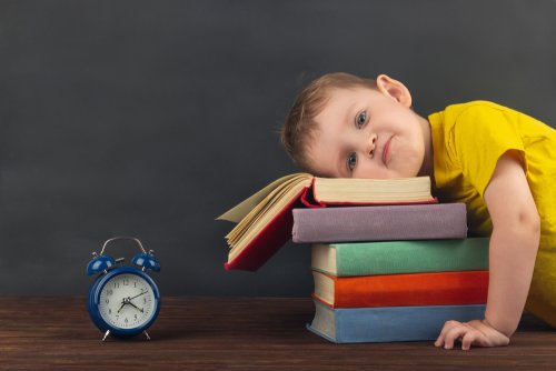 Niño con la cabeza sobre unos libros y un reloj despertador.