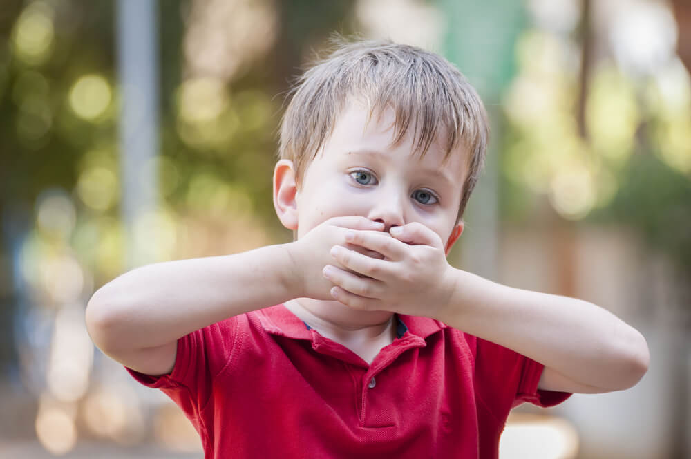 Ett barn som täcker sin mun med händerna.