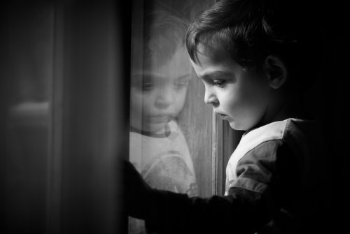 Niño mirando por la ventana muy triste tras la pérdida de un ser querido.