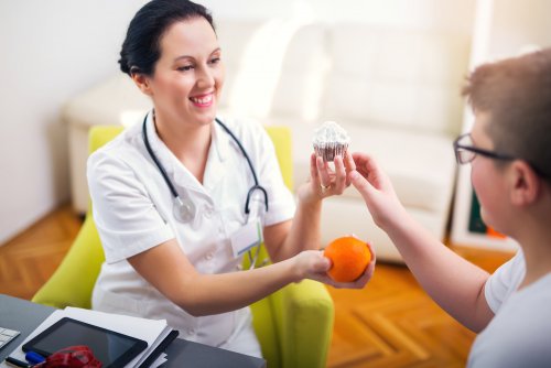 Nutricionista intercambiando con un niño un pastel por una fruta.