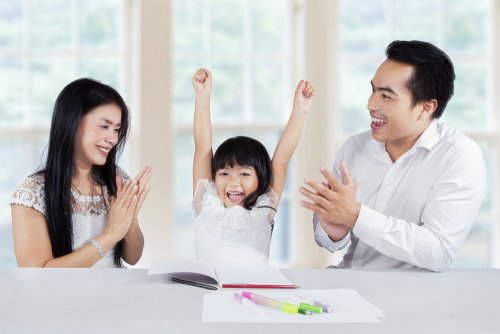 Padres felicitando a su hija por haber hecho bien las tareas escolares en casa de una forma divertida.