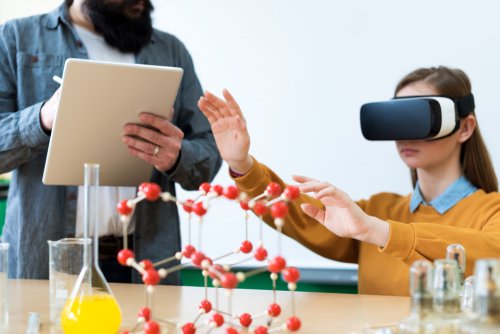 Niña en el aula utilizando la realidad virtual y aumentada con su profesor tomando notas.