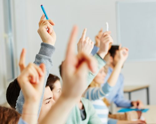 Alumnos levantando la mano en clase para aprender.