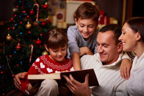Familia leyendo libros sobre la Navidad junto al árbol.