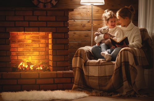 Madre leyendo cuentos para relajarse a tu hija junto a la chimenea.