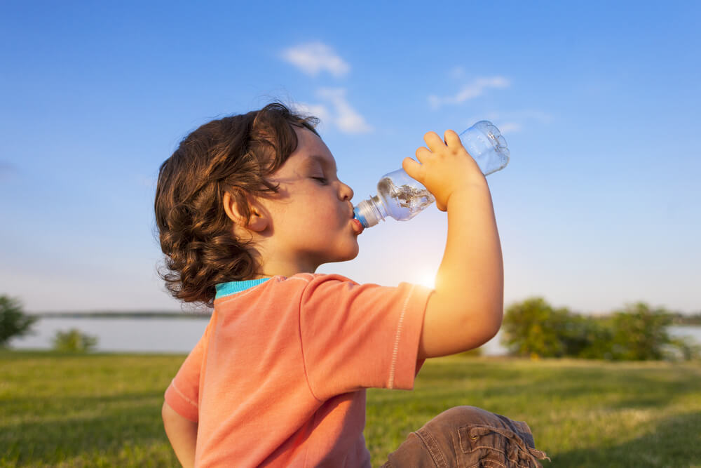 A child sitting in the grass drinking a bottle of water.