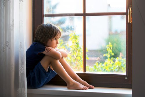 Niño triste mirando por la ventana.