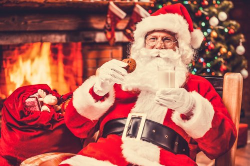 Papá Noel comiendo galletas y leches frente a una chimenea.