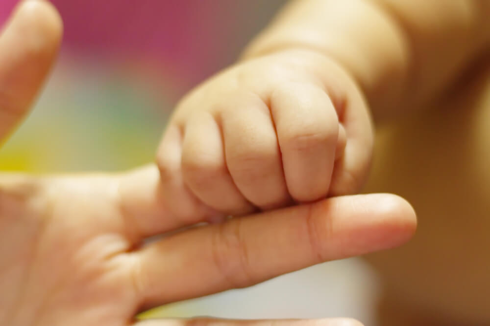 Bebé agarrando el dedo de su madre, su principal figura de apego.