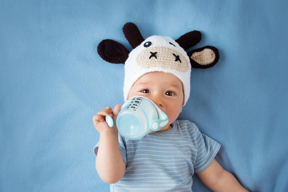 A baby drinking baby formula from a sippy cup.