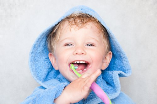 Niño lavándose los dientes con el albornoz puesto.