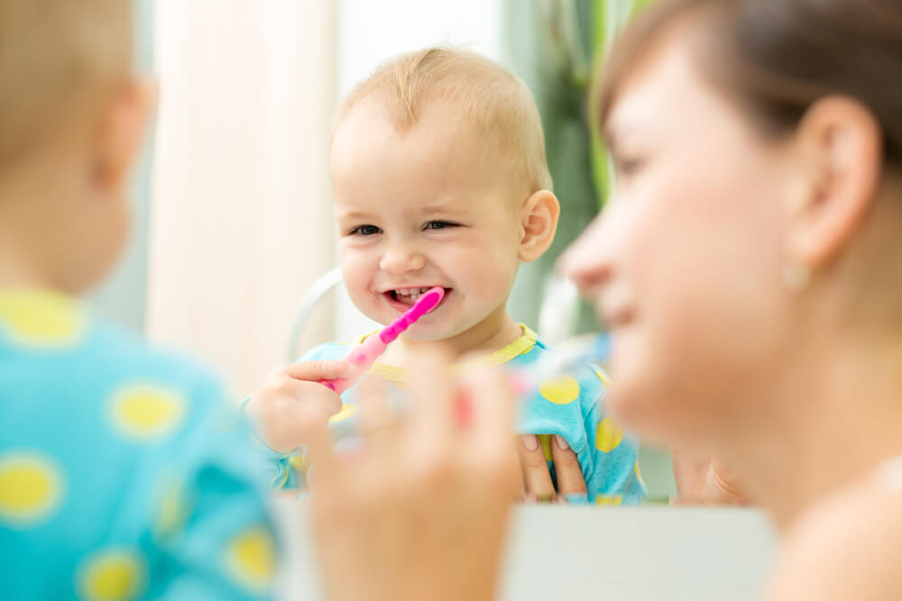 Enfant avec sa mère apprenant à se brosser les dents.